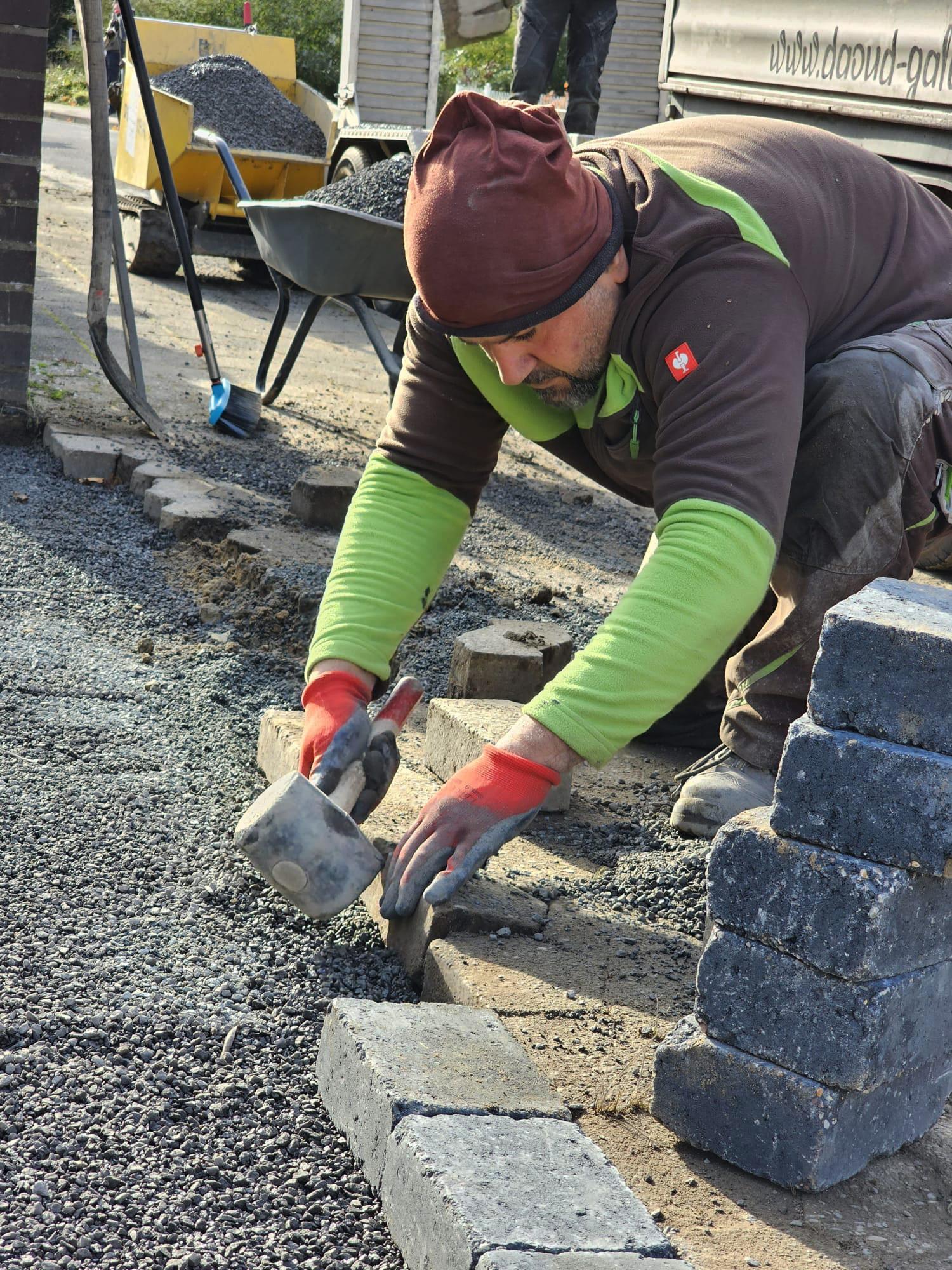 Bazid Daoud setzt Pflastersteine mit dem Gummihammer auf einer Baustelle